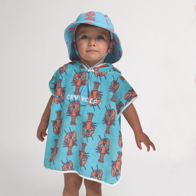 Child wearing a blue poncho towel with red lobster pattern and matching hat on a white background
