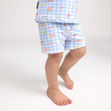 Child wearing light blue checkered swim shorts with colourful patterns on a white background