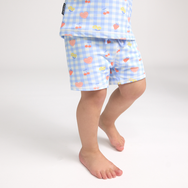 Child wearing light blue checkered swim shorts with colourful patterns on a white background