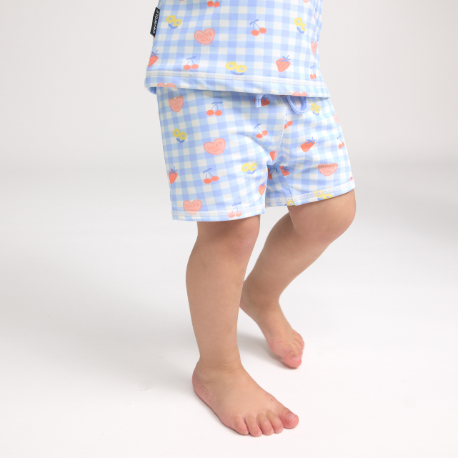 Child wearing light blue checkered swim shorts with colourful patterns on a white background
