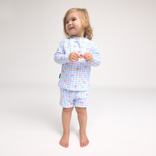 Child wearing a light blue checkered swim set with all over fruit pattern