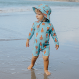 Child wearing a light blue swimsuit and swim bucket hat with orange lobster pattern on a beach