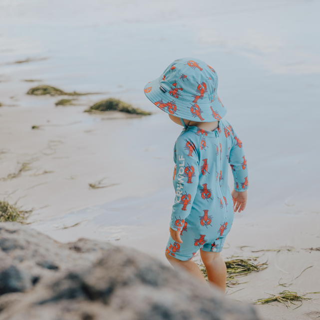 Child wearing a blue swimsuit with red patterns and matching hat on a beach.