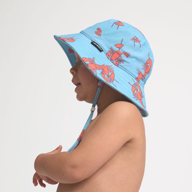 Child wearing a blue sun hat with red lobster pattern on a light gray background