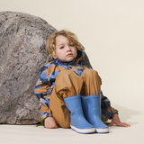 Child sitting against rock wearing the CRYWOLF Play Jacket Camo Mountain and Southern Blue rain boots