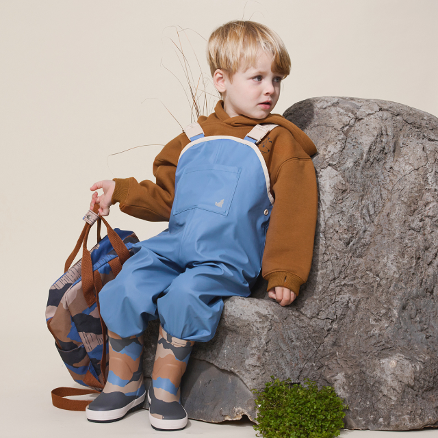 Child sitting on rock wearing CRYWOLF Rain Overalls Southern Blue - studio shot