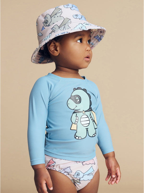 Child wearing the HUXBABY Super Dino Swim Nappy and matching swim hat