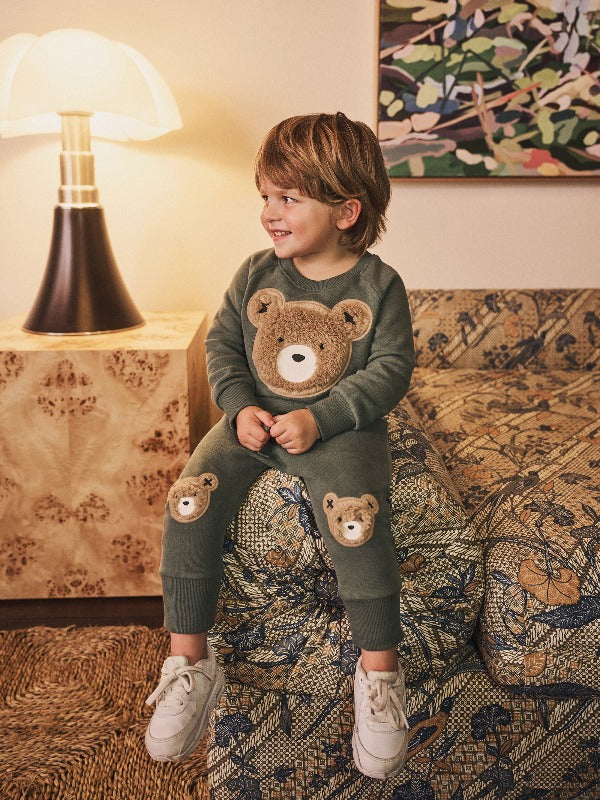 Child sitting on couch wearing the HUXBABY Light Spruce Furry Huxbear Sweatshirt and drop crotch pant