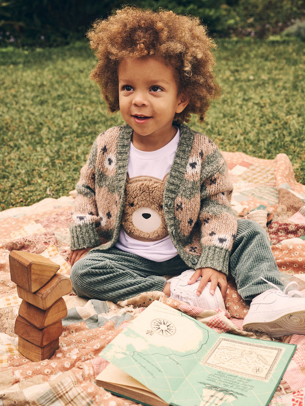 Child sitting down wearing the HUXBABY Light Spruce Huxbear Boxy Cardi with the Huxbear tee underneath and the Light Spruce Cord Pant