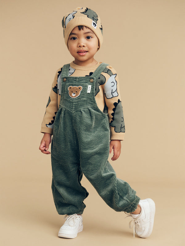 Child wearing the HUXBABY T-Rex Knit Beanie and matching knit sweater and Orchid cord overalls