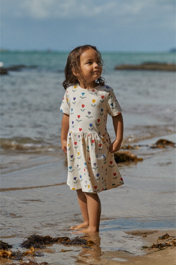 Young girl in a flower patterned dress standing on a beach with ocean in the background