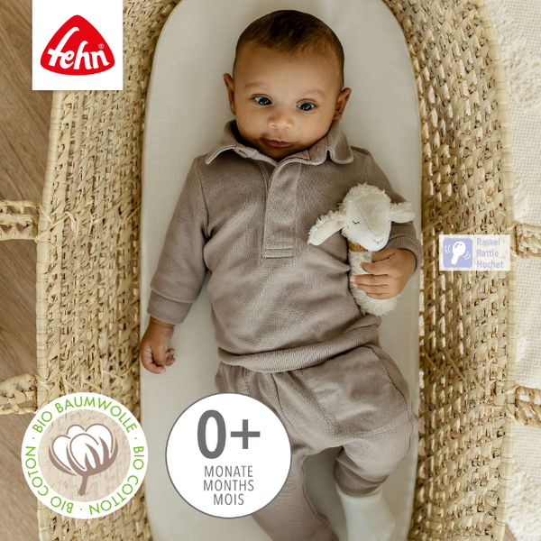 Baby in a beige outfit holding a toy, standing in a woven basket with Fehn branding.