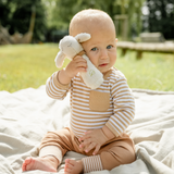 Baby in a striped outfit holding a plush toy outdoors