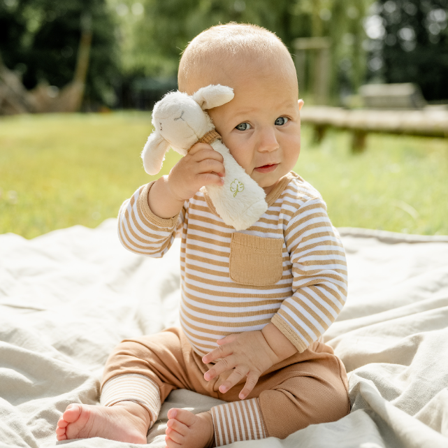 Baby in a striped outfit holding a plush toy outdoors