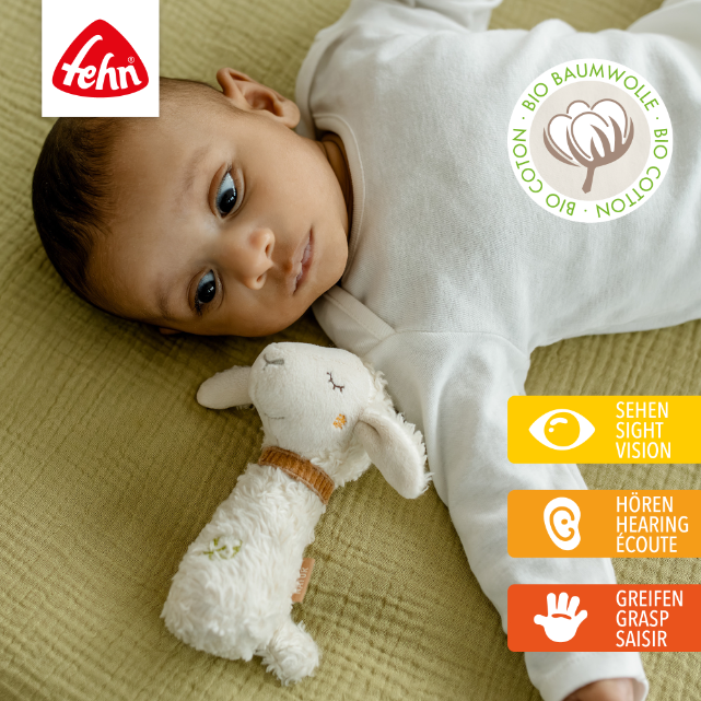 Baby lying on a green blanket with a white toy, wearing a white onesie, with Fehn logo and bio cotton certification.