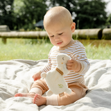 Baby sitting on a blanket outdoors holding a plush toy