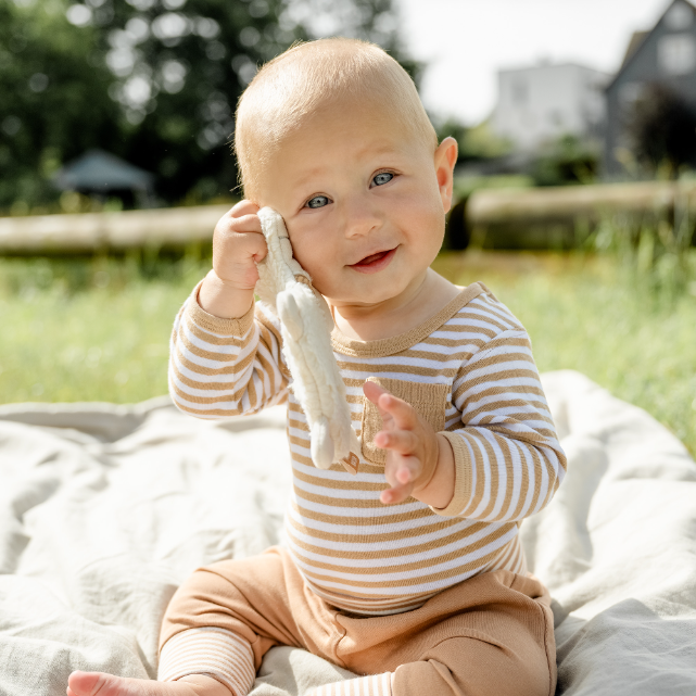 Baby sitting outdoors on a blanket holding a toy