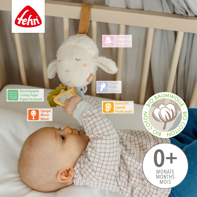 Baby playing with a toy sheep in a crib, with Fehn branding visible.