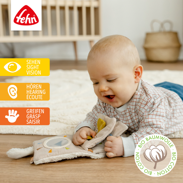 Baby playing with a soft book on a wooden floor, with 'fehn' brand logo and sensory development icons.