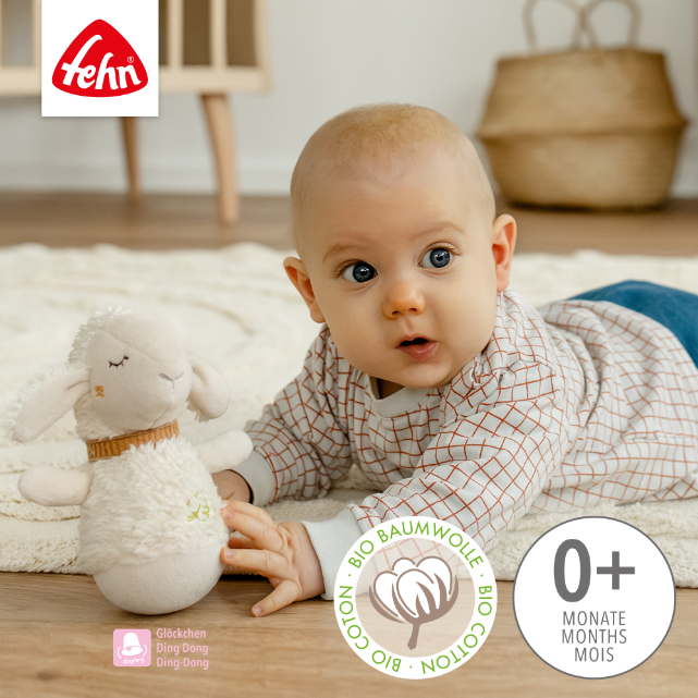 Baby playing with a soft toy sheep in a cozy room, featuring the Fehn brand logo.