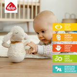 Baby playing with a plush toy sheep on a wooden floor, with the Fehn brand logo visible.
