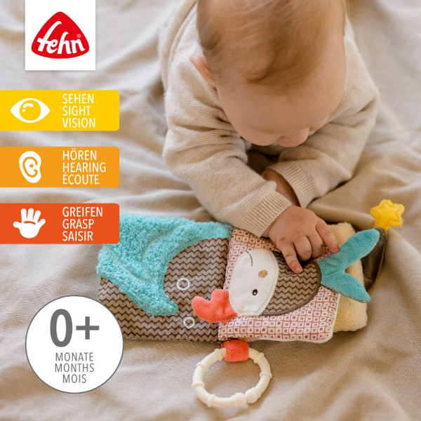 Baby playing with a soft toy book, featuring the Fehn brand logo.