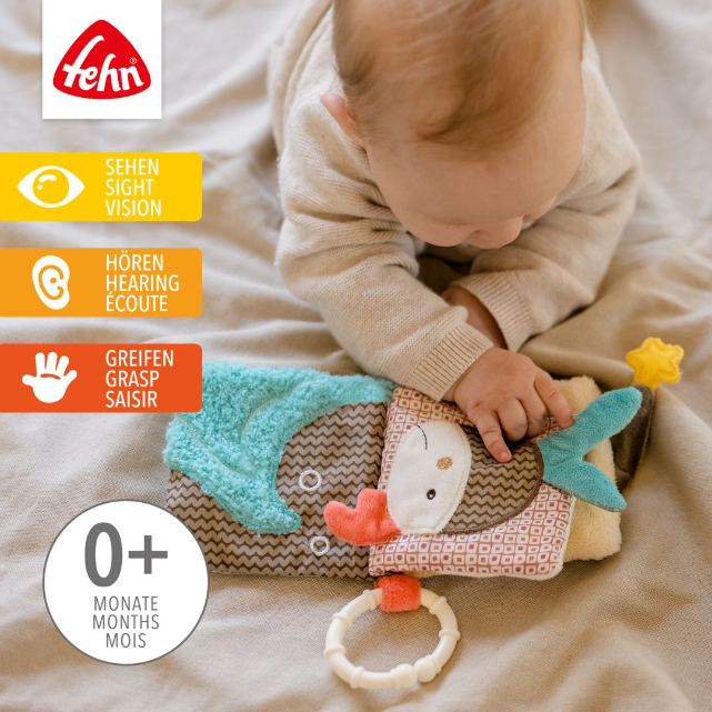 Baby playing with a soft toy book, featuring the Fehn brand logo.
