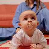 Baby lying on floor sucking on a pink dummie