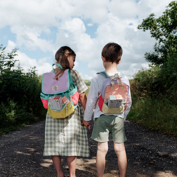 Two children wearing backpacks with Olli Ella Playpa Minis in the pockets