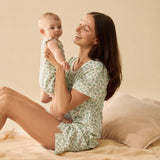 Woman and baby in matching green floral pajamas sitting on a bed.