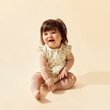 Baby sitting on a beige background wearing a lemon leaf print romper.