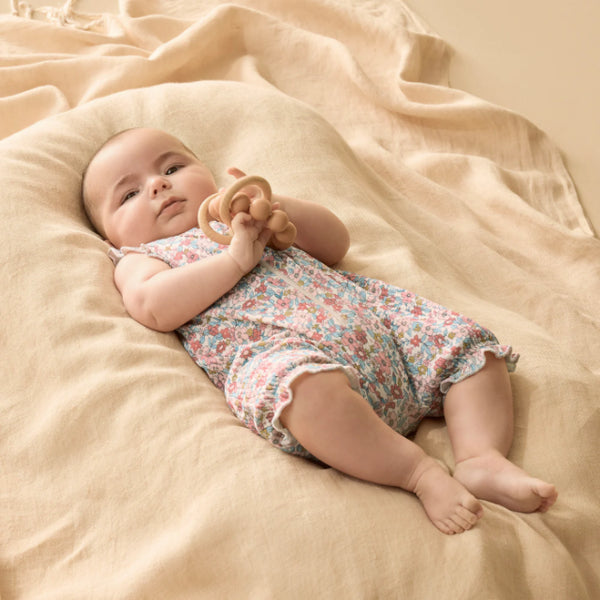 Baby in a floral romper lying on a beige blanket