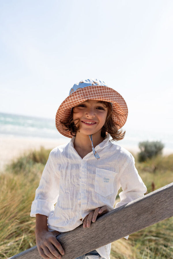 CHILD AT BEACH WEARING ACORN Platapus Wide Brim Bucket Hat WITH THE BRIM FOLDED UP SHOWING THE CHESTNUT CHECKED UNDERSIDE