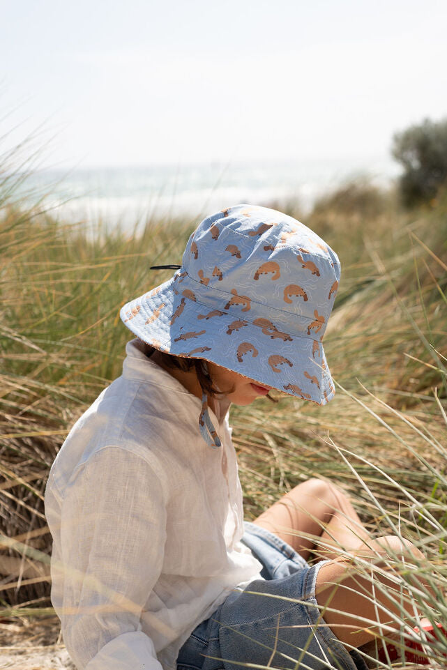 SIDE VIEW OF CHILD SITTING DOWN WEARING ACORN Platapus Wide Brim Bucket Hat