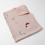 Pink knitted blanket with animal and mushroom designs on a white background