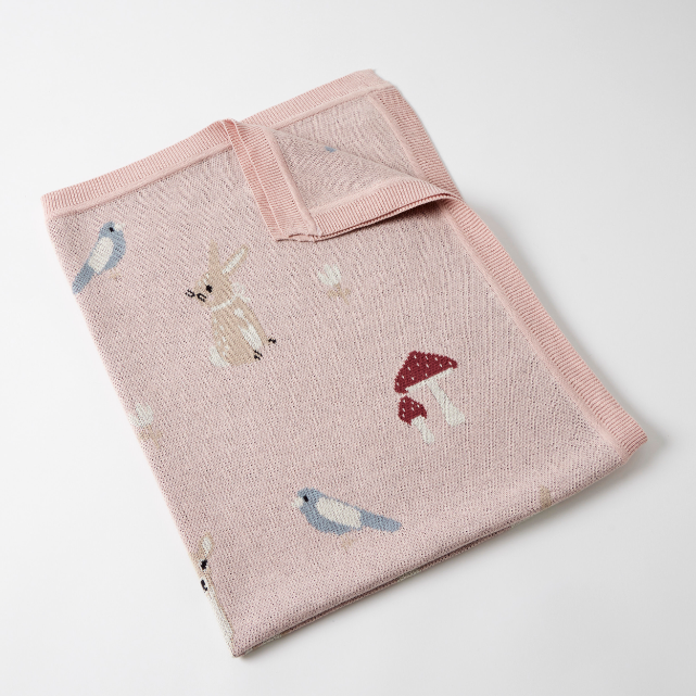 Pink knitted blanket with animal and mushroom designs on a white background