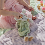 Child in a pink dress holding a plush toy mouse on a textured surface with cupcakes in the background.