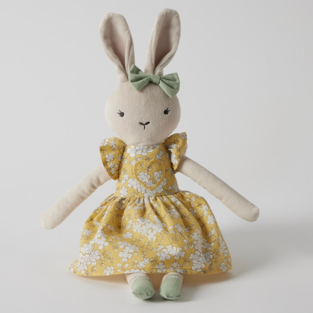 Stuffed bunny toy with a yellow floral dress and green bow on a white background