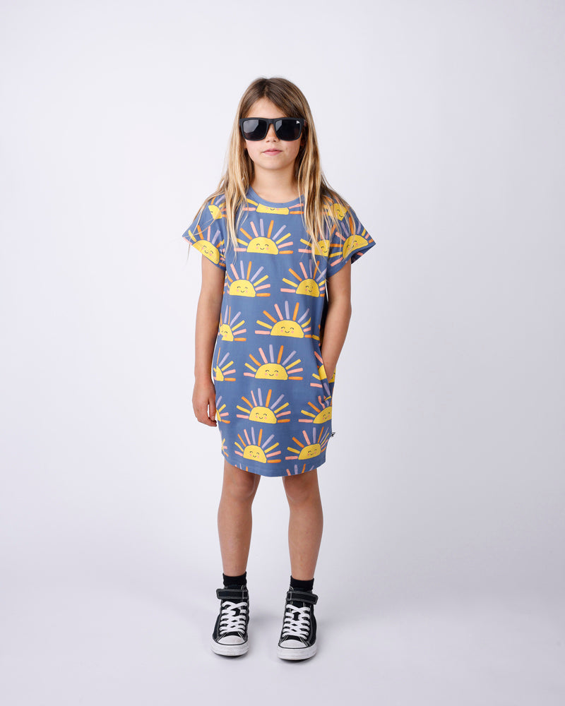 Child wearing a dress with sun pattern and sunglasses on a white background
