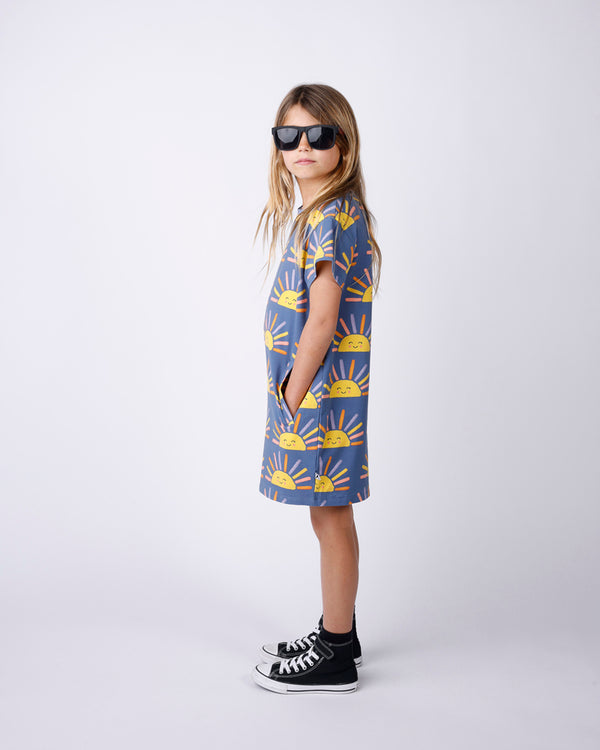 Child wearing a patterned dress with black sunglasses on a white background