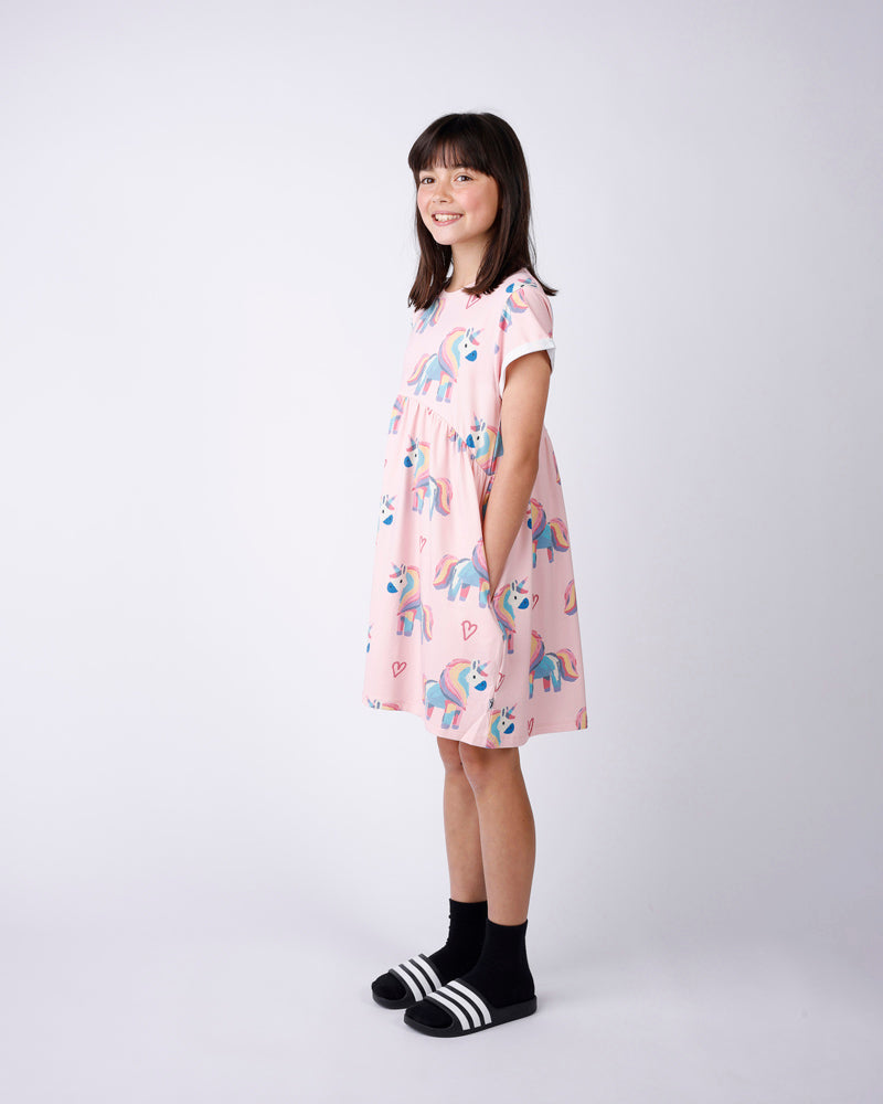 Young girl wearing a pink dress with unicorn print on a white background