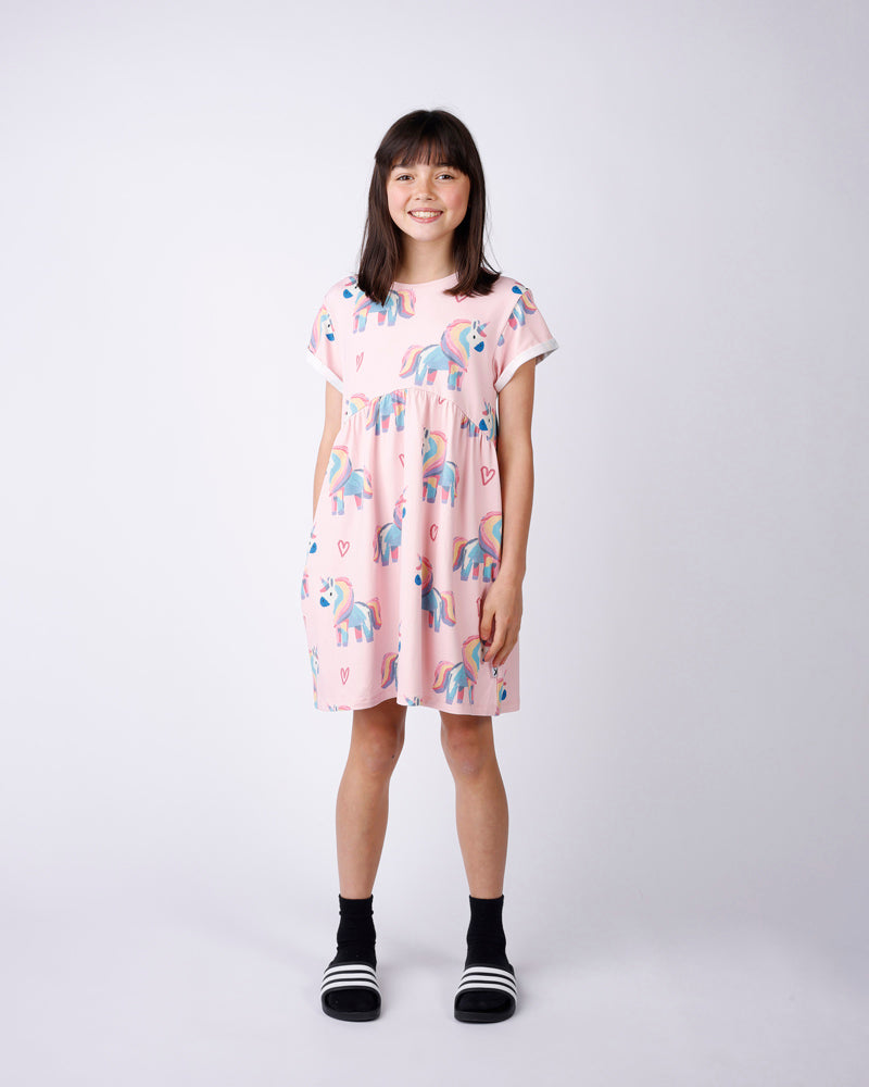 Young girl wearing a pink dress with unicorn print on a white background