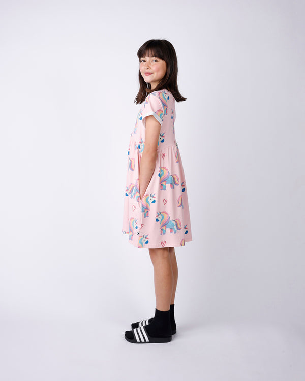 Side view of a Young girl wearing a pink dress with unicorn print on a white background