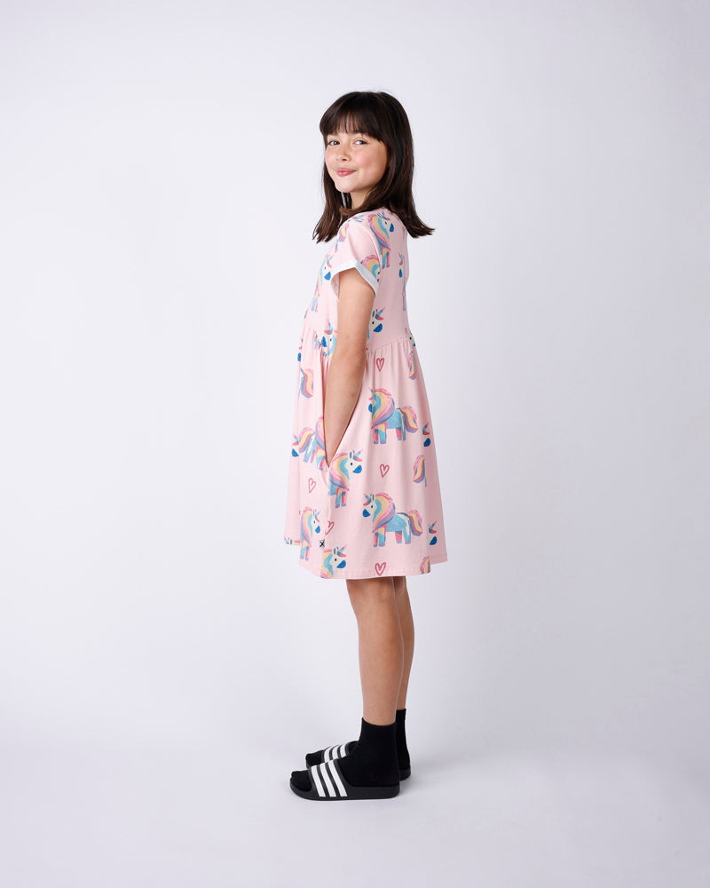 Side view of a Young girl wearing a pink dress with unicorn print on a white background