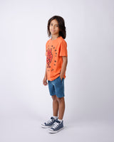 Child wearing an orange t-shirt with a graphic design and blue shorts on a white background