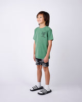 Child wearing a green t-shirt and black shorts with white patterns on a white background