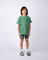 Child wearing a green t-shirt and black shorts with white skull patterns on a white background