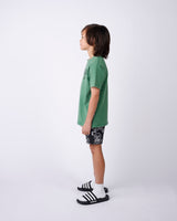 Child wearing a green t-shirt and black shorts with white patterns on a white background