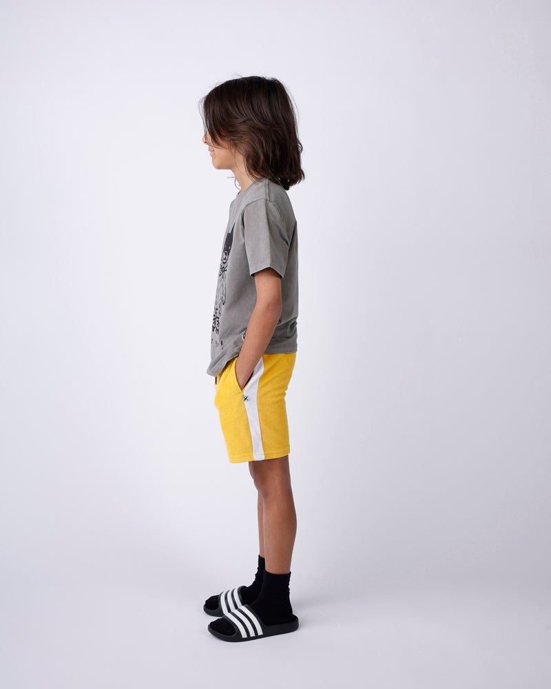 Child wearing a gray t-shirt, yellow shorts, and black shoes on a white background