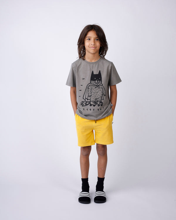 Child wearing a gray t-shirt with a graphic design and yellow shorts on a white background
